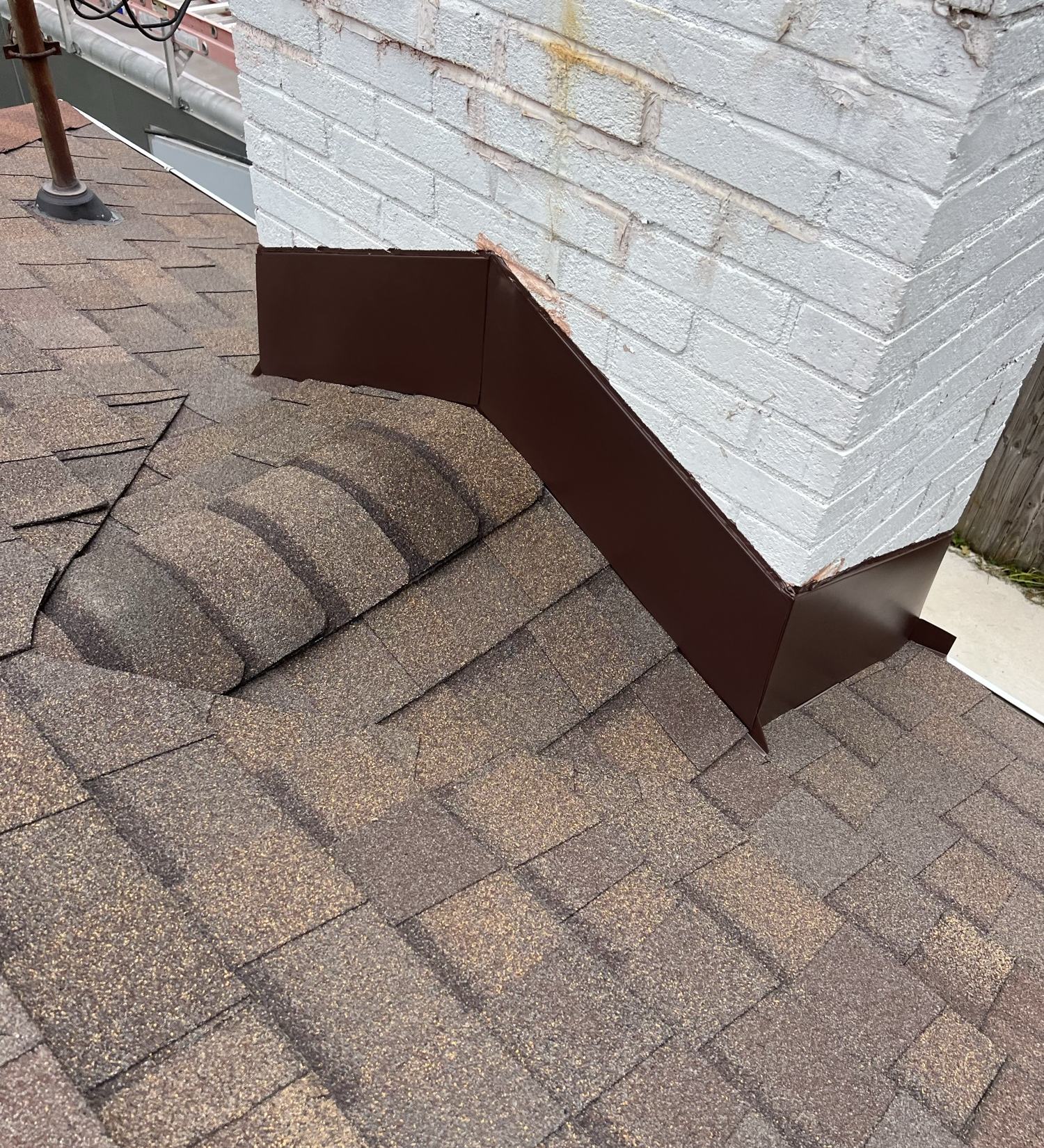 New metal flashing installed where a shingle roof meets a brick chimney