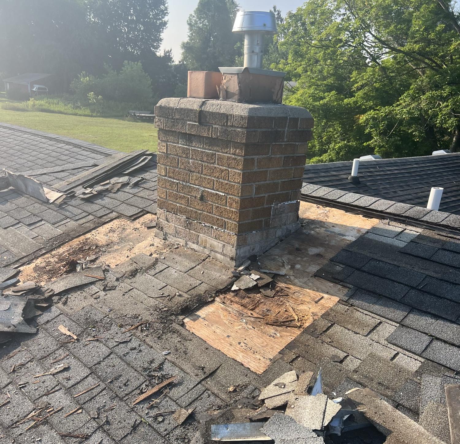 Shingles and rotted roof decking torn off around a chimney to trace a roof leak