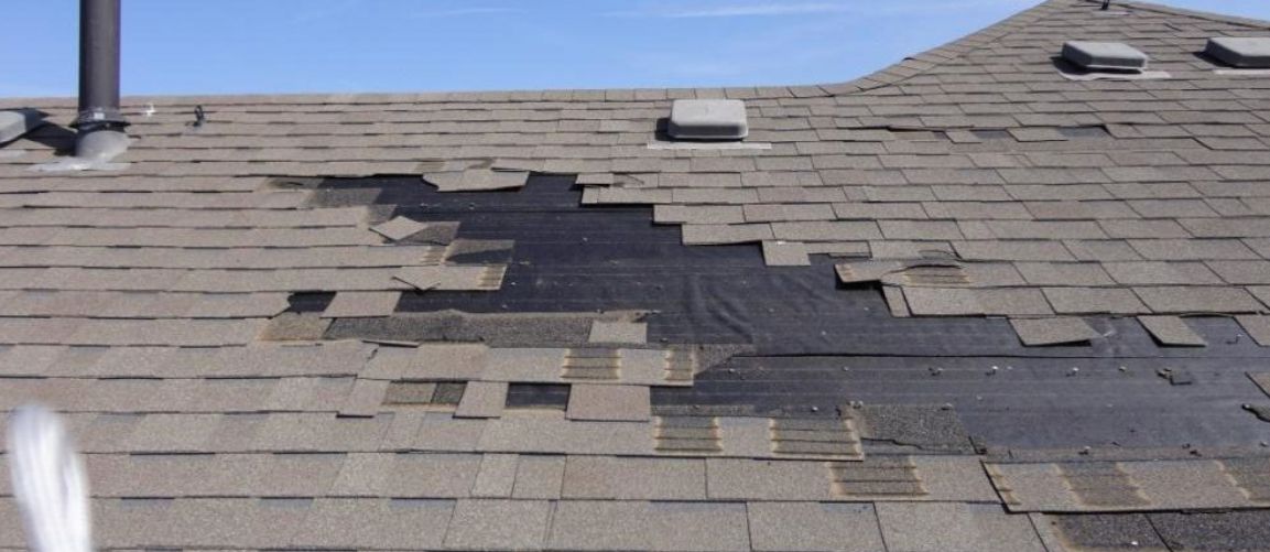 Asphalt shingles torn off by wind, exposing the underlayment